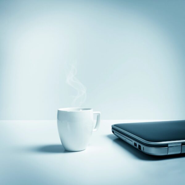 Closed laptop with mug of hot tea, coffee, blue toned